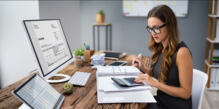 Bookkeeper working at a desk with a calculator and computer.