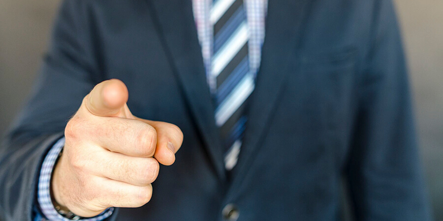 Close up of a man in suit pointing at the viewer.