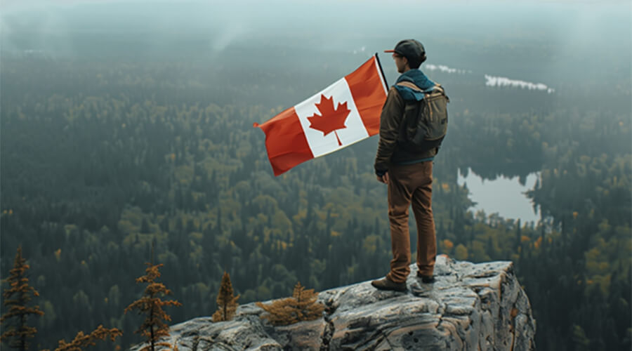 Man standing on the summit of a mountain with a Canadian flag.