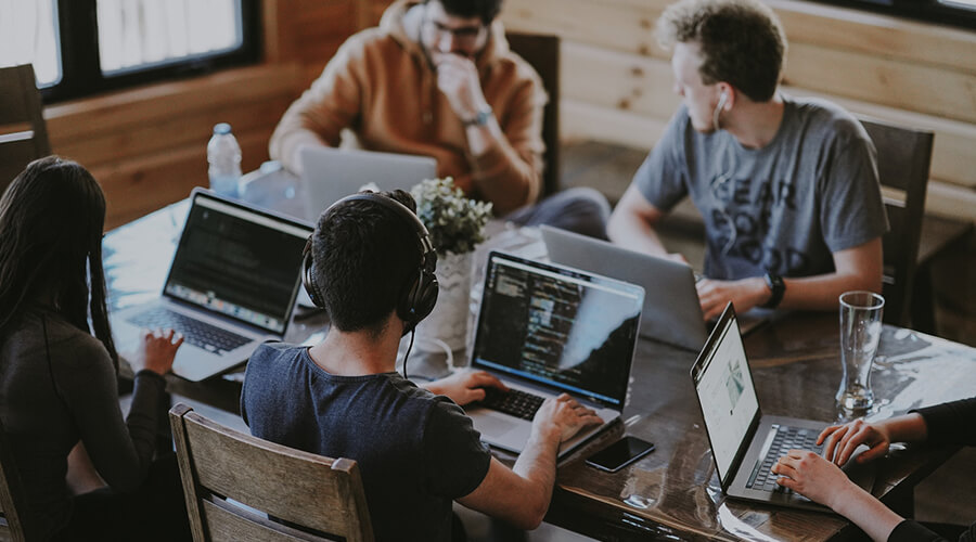 Group of people working on laptops around a table.