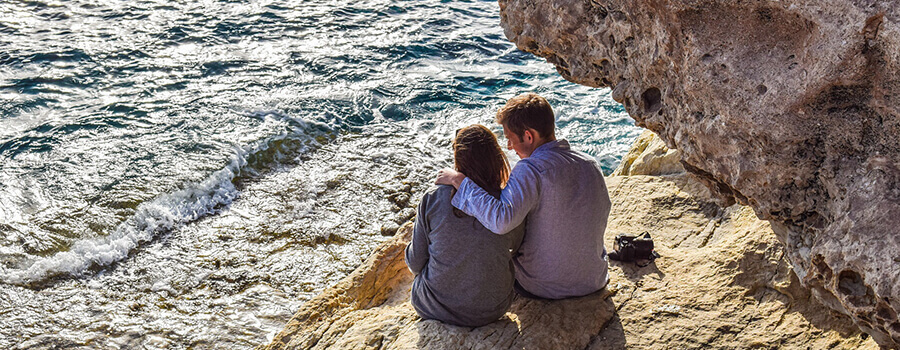 Couple communicating on rocks by the ocean.