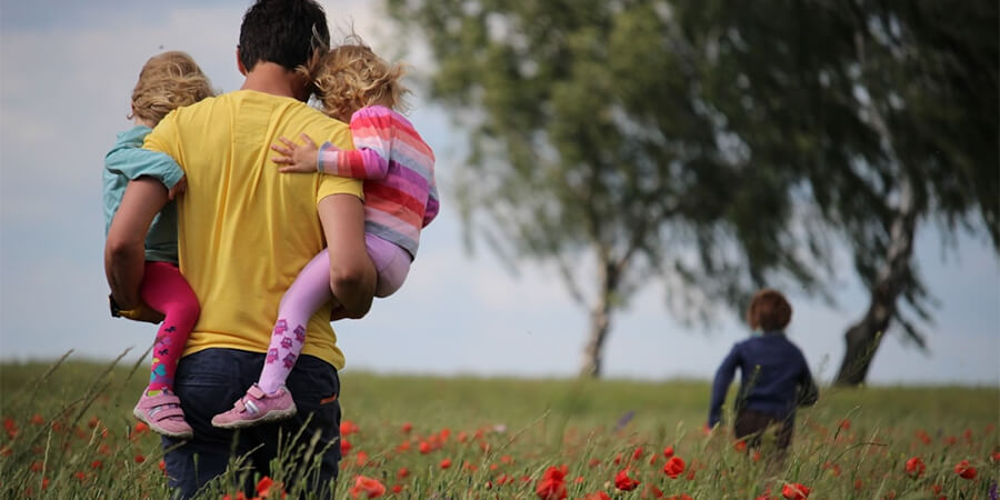 Dad carrying two small children in a poppy field.