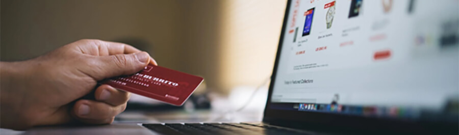 Male hand holding a credit card over a laptop.