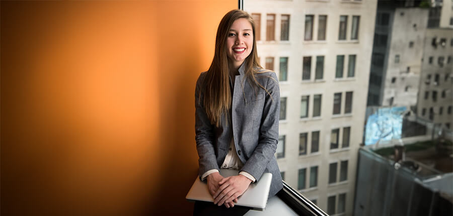 Business woman sitting in the window of a skyscraper with an orange wall.