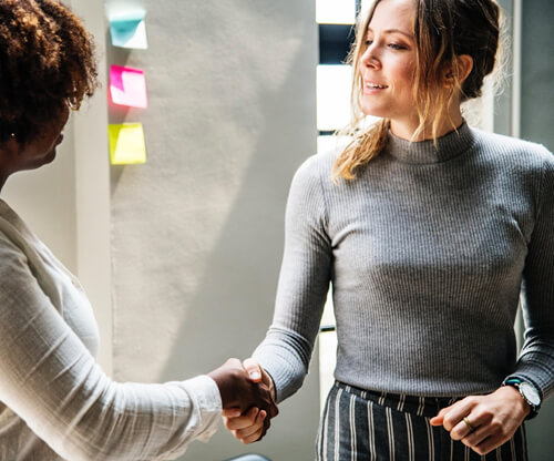 Two young professional women shaking hands.