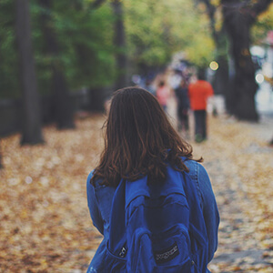 Girl with a back pack walking down a city avenue.