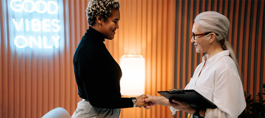 Two women shaking hands. Neon sign reads 'Good Vibes Only'