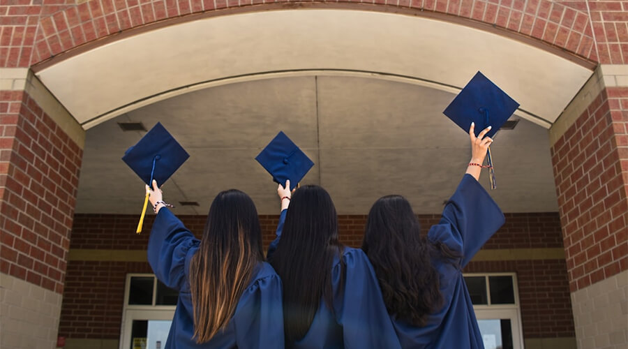 Graduates in blue gowns holding up their motar boards