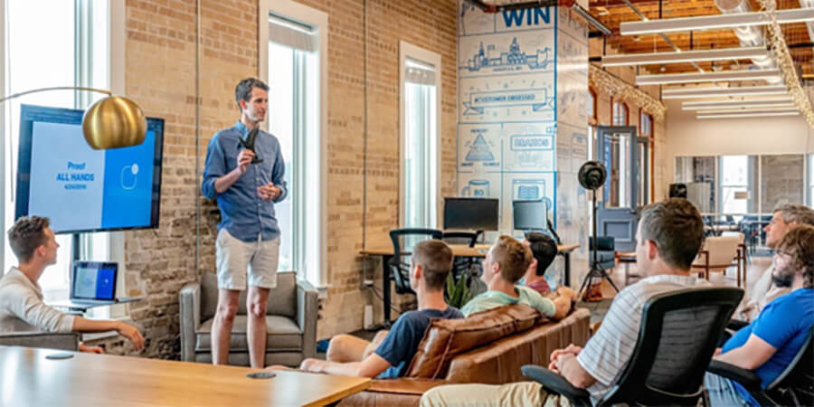 Man wearing shorts presenting to a group in a modern office.