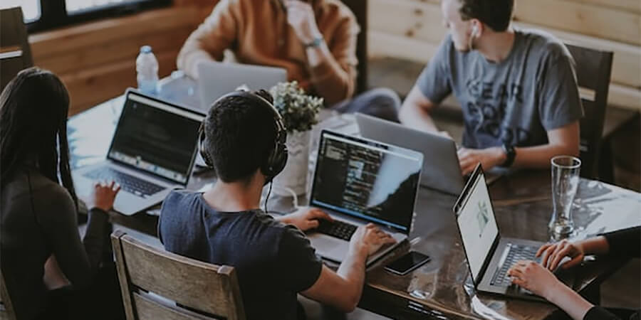 Group of professionals working on laptops around a wooden table.