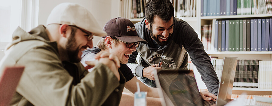 Three men laughing at something on a laptop.