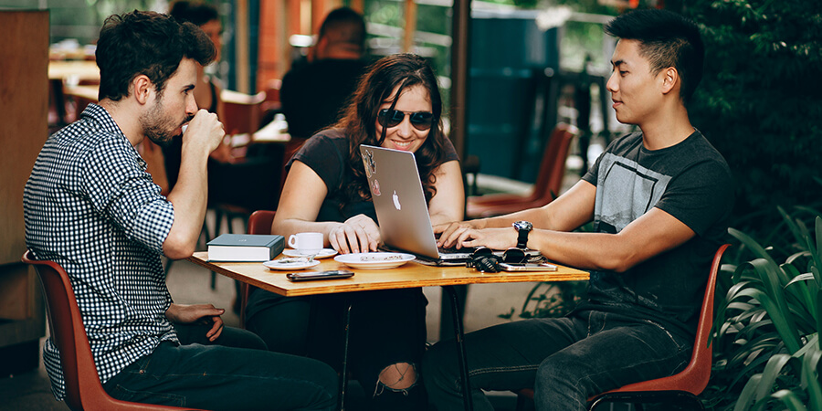 Three people sitting around a table in a cafe with a laptop.