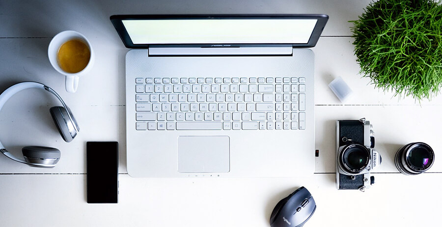 Headphones and an analog camera next to a laptop and phone on a table.