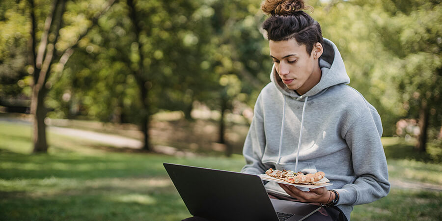 Person sitting on a bench in the park with their lunch and a laptop.