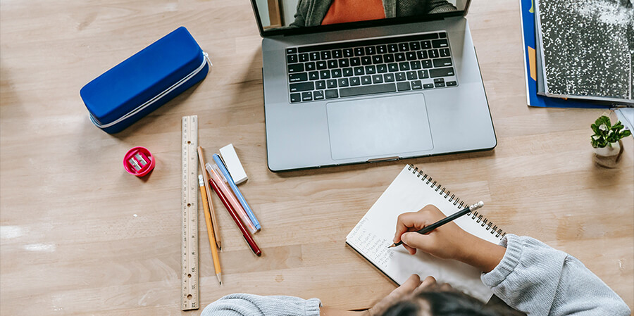 Making notes in a notebook with a laptop on a desk.