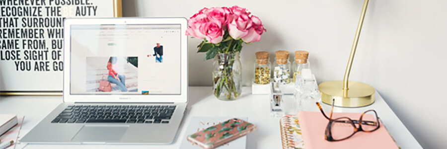 Desk with laptop, flowers, poster and glasses.