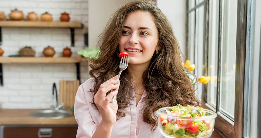 Woman eating a salad in her kitchen.