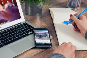 A person studying promotional content on laptop and cell phone.