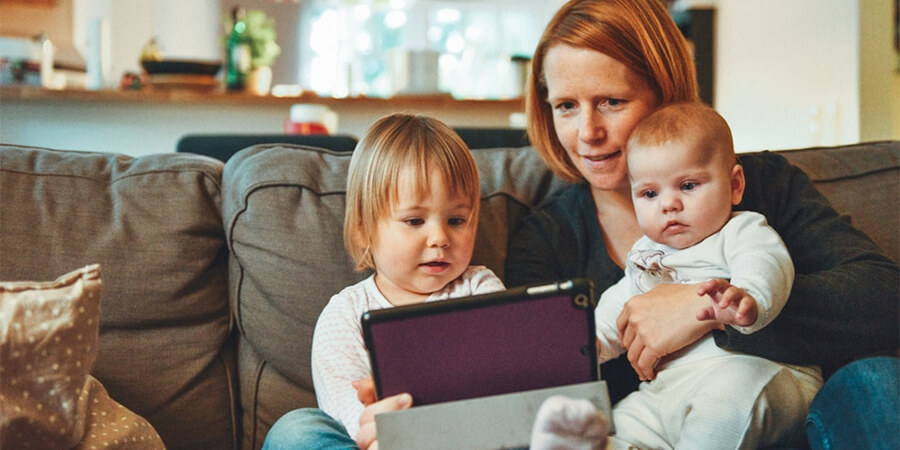 Mother and young daughters oin sofa looking at a tablet