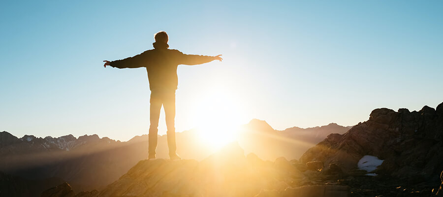 Man standing on top of a mountain with his arms outstretched during sunrise.