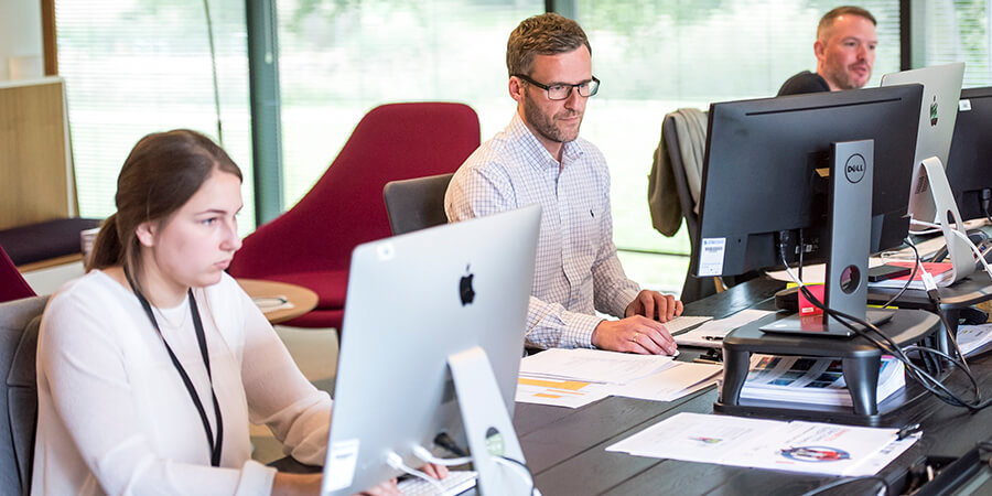 Group of three people working on computers in an office.