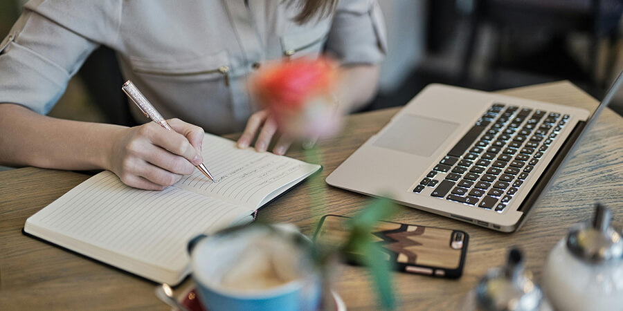 Woman writing in a notepad on a desk.