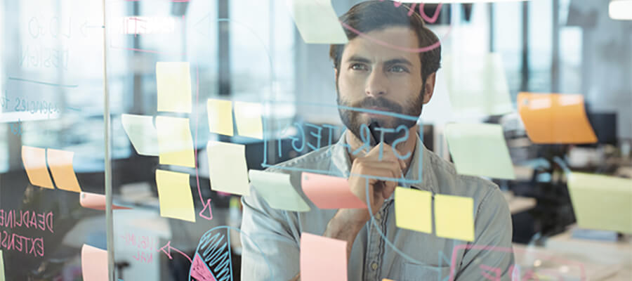 Man pondering post-it notes on a glass partition.