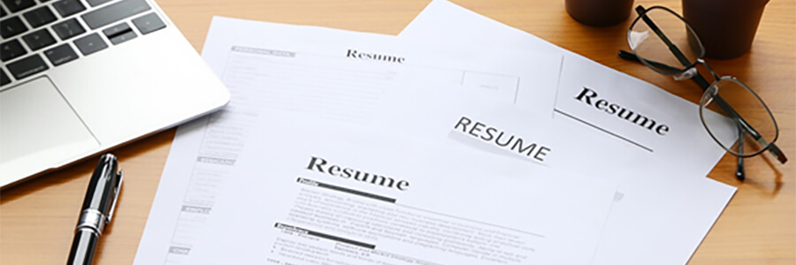 Copies of a resume with laptop, pen and glasses.