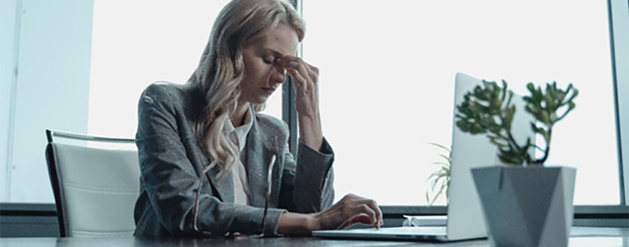 Woman clutching the bridge of her nose with one hand on laptop.