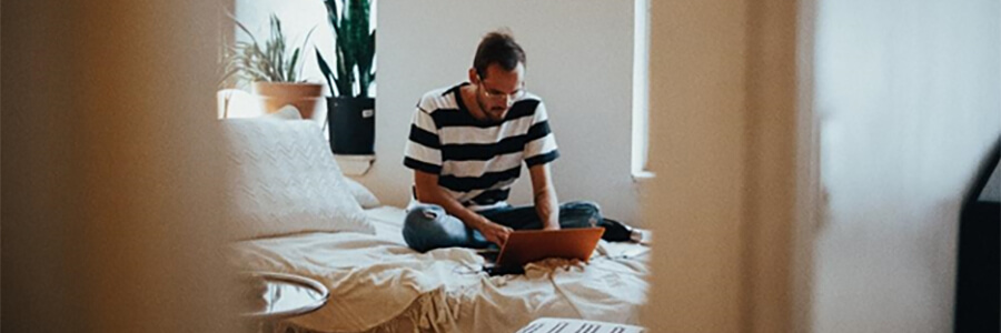 Man sitting on a bed using a laptop.