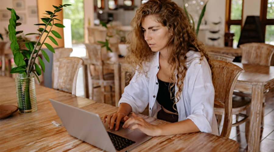 Woman working on a laptop on a large wooden table.