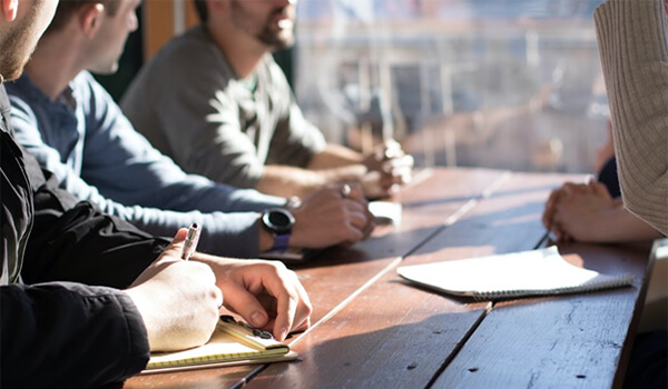 Group of people meeting around a wooden table.